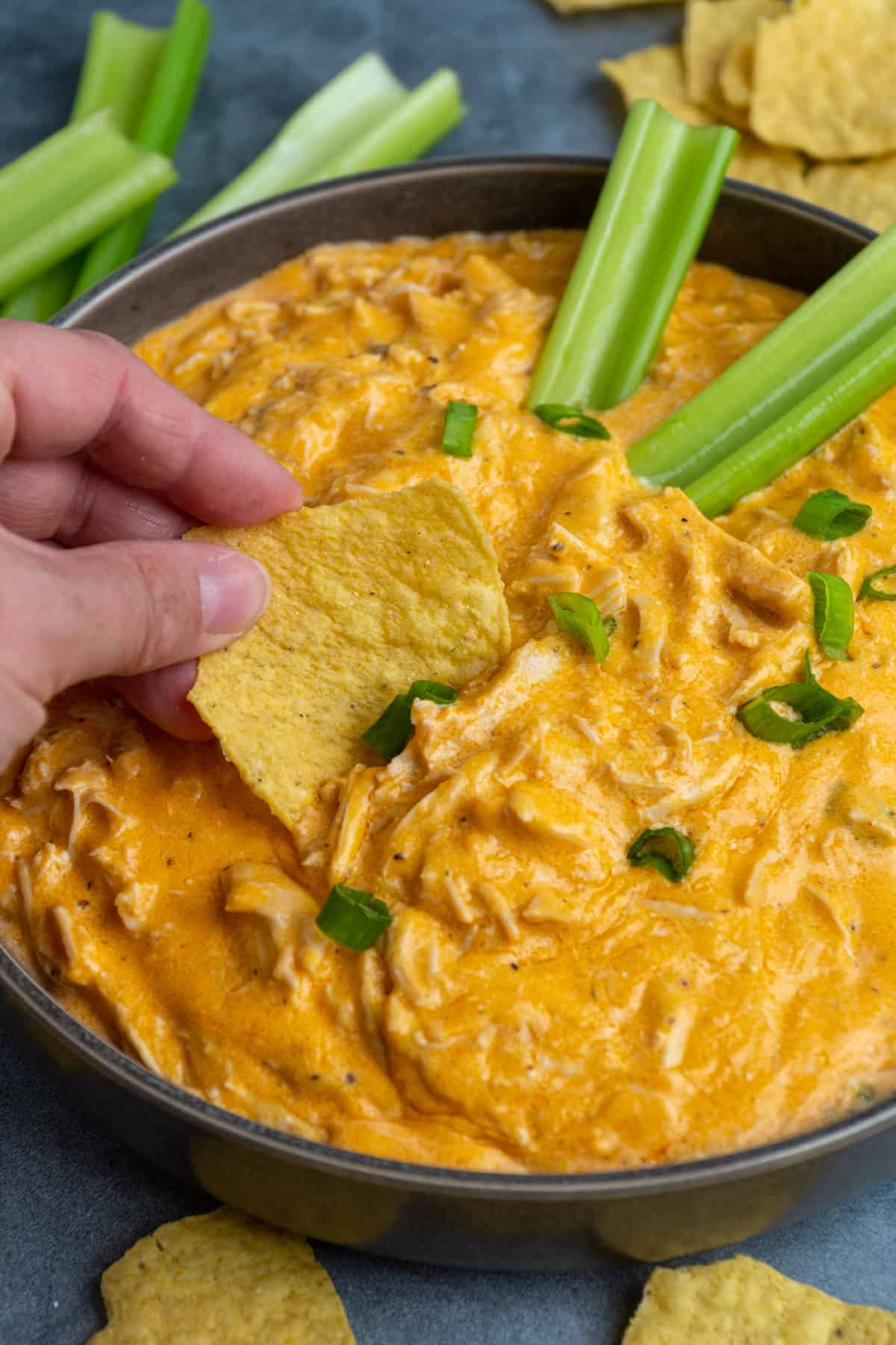 Close up of buffalo chicken dip in a grey bowl with a chip being dipped in it.