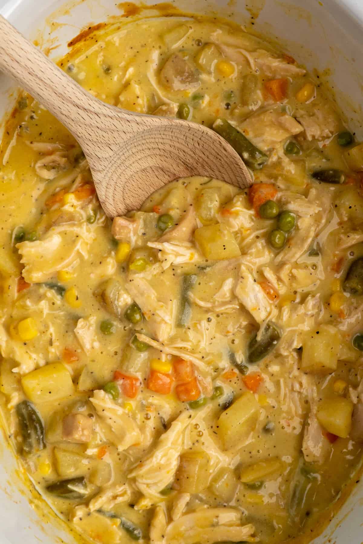 Chicken pot pie mixture with a wooden spoon in it inside a slow cooker.