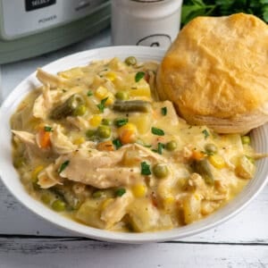 Crock Pot chicken pot pie in a white bowl with a biscuit in it and a slow cooker in the background.