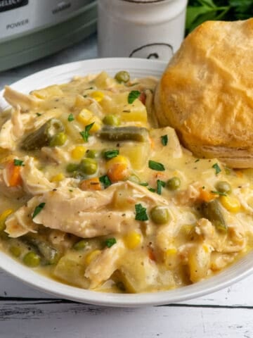 Crock Pot chicken pot pie in a white bowl with a biscuit in it and a slow cooker in the background.