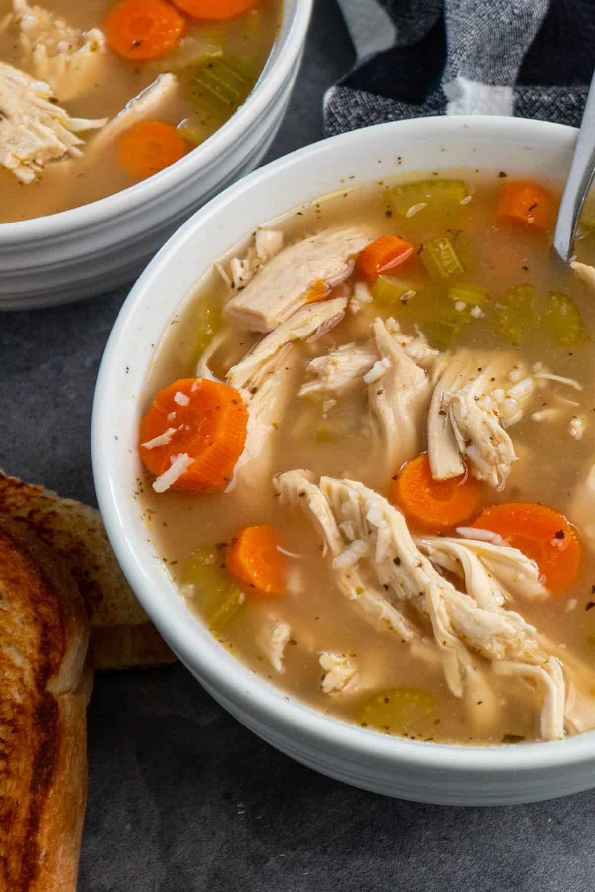 Close up of Crock Pot chicken and rice soup in a white bowl with a grilled cheese sandwich.