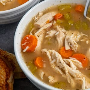 Close up of Crock Pot chicken and rice soup in a white bowl with a grilled cheese sandwich.