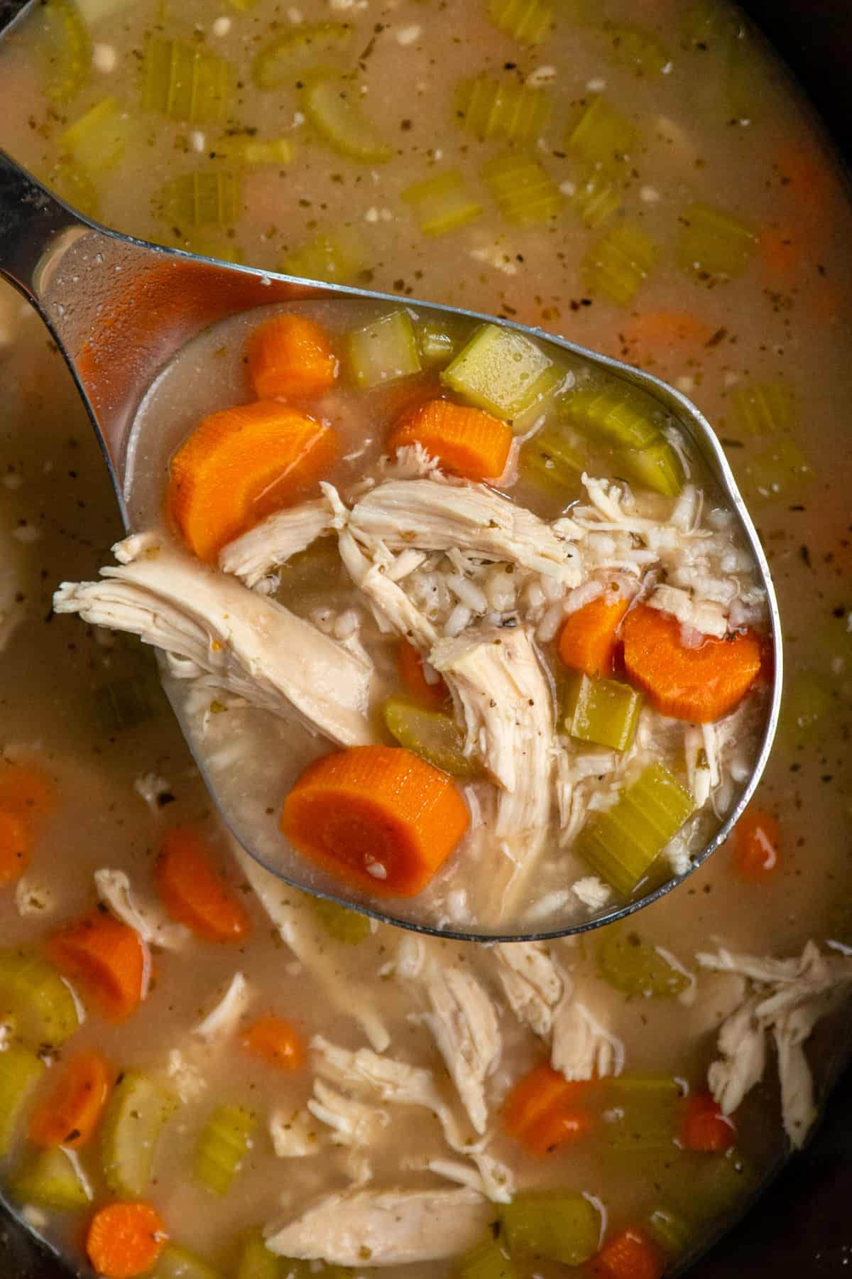 Overhead look at chicken and rice soup in a laddle over a slow cooker.
