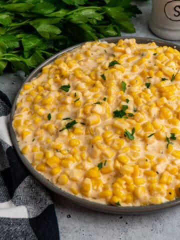 Crock pot creamed corn in a grey dish topped with fresh parsley.