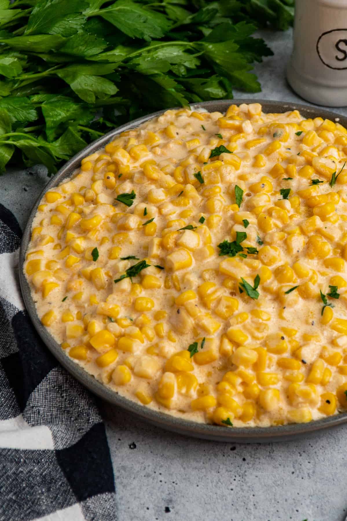 Crock pot creamed corn in a grey dish topped with fresh parsley.
