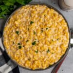 Crock pot creamed corn in a grey dish topped with fresh parsley.