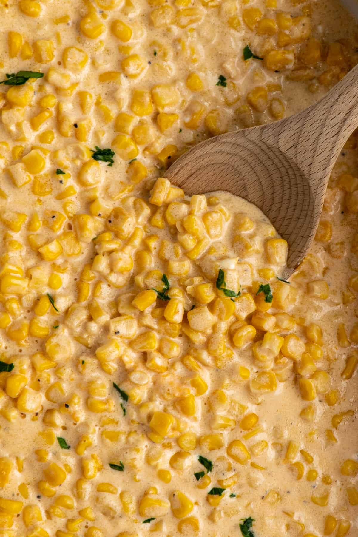 Creamed corn in a slow cooker with a wooden spoon.