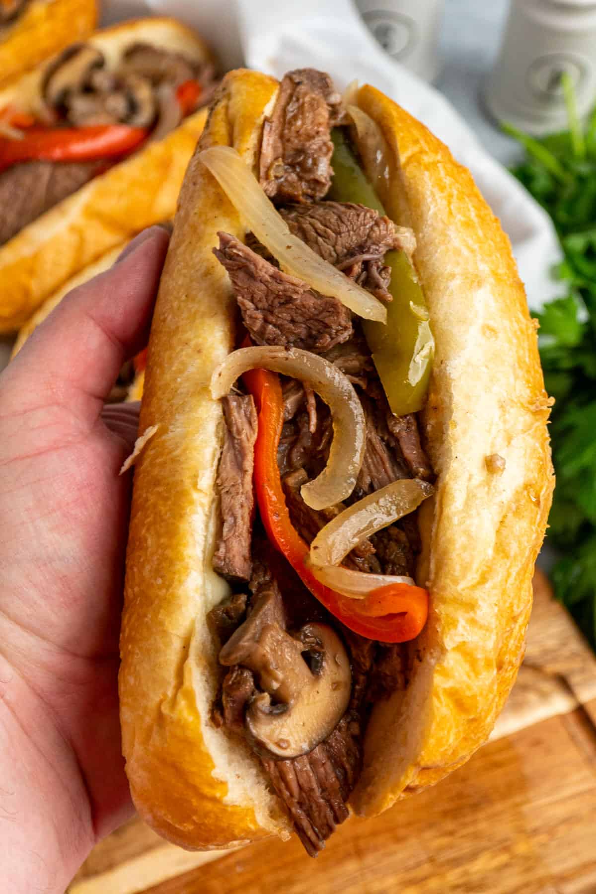 A hand holding a Philly cheesesteak sandwich in a hoagie roll.