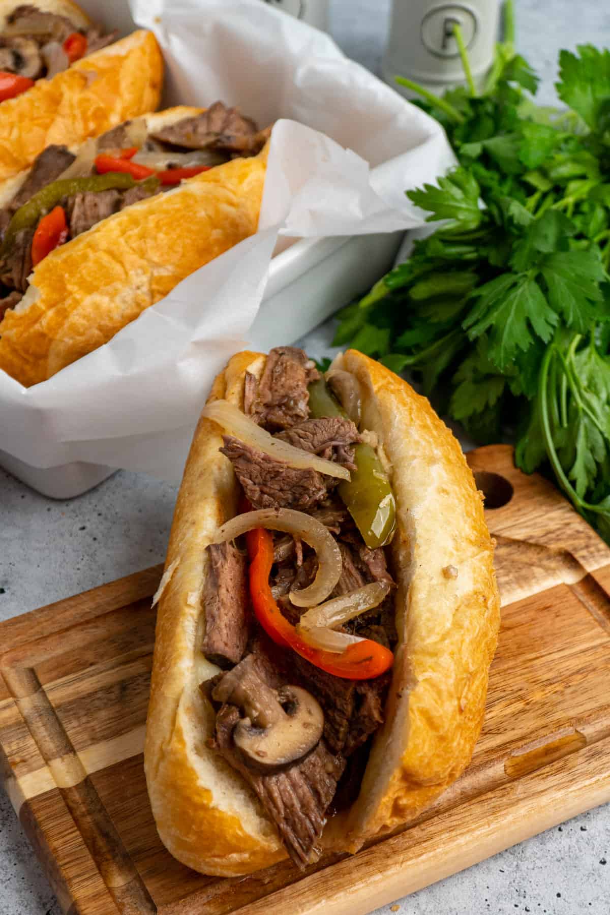 Crock Pot Philly cheesesteak sandwiches in a hoagie roll on a wood cutting board.