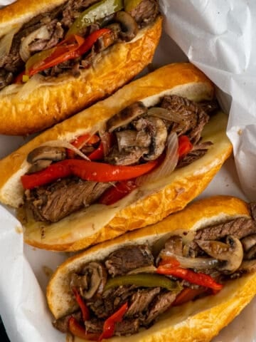 Crock Pot Philly cheesesteak sandwiches in a baking dish lined with parchment paper.