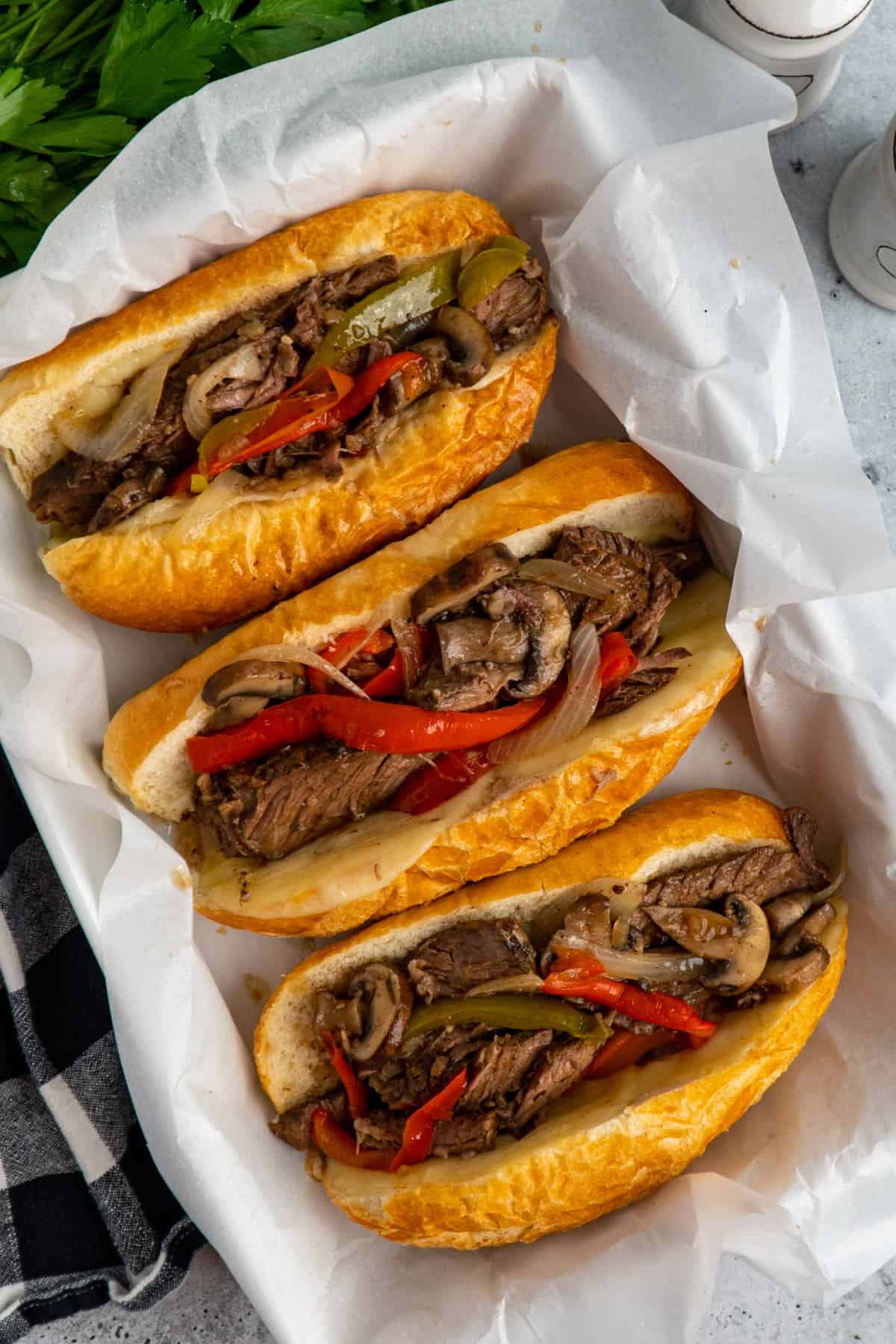 Crock Pot Philly cheesesteak sandwiches in a baking dish lined with parchment paper.