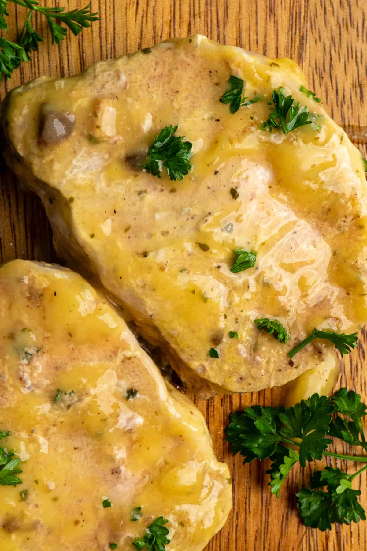 Close up of Crock Pot pork chops on a wood cutting board with fresh parsley