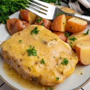 Crock Pot ranch pork chops on a plate with red potatoes and garnished with parsley.