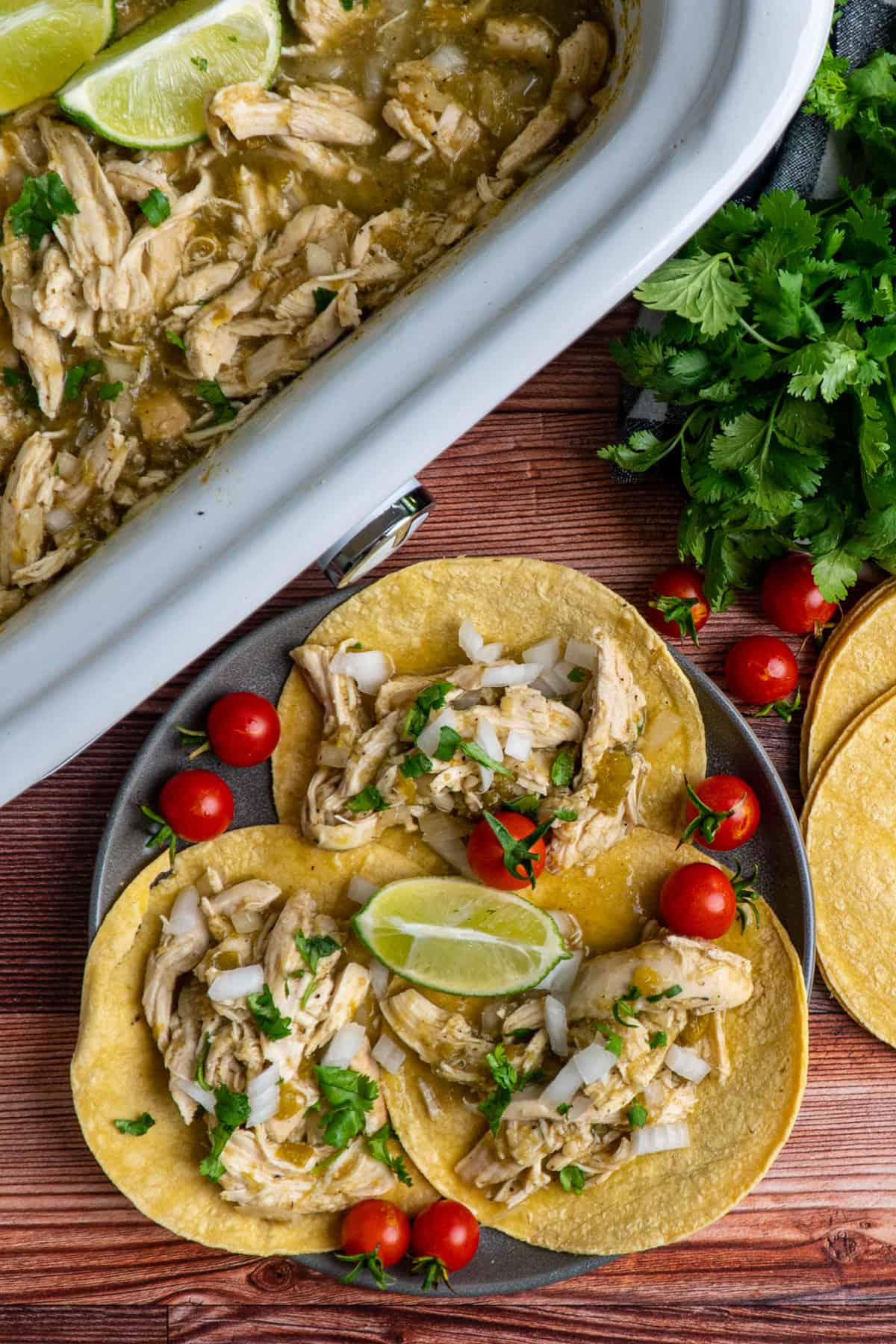 Three corn tortillas with Salsa Verde chicken on them and garnished with tomatoes and limes.