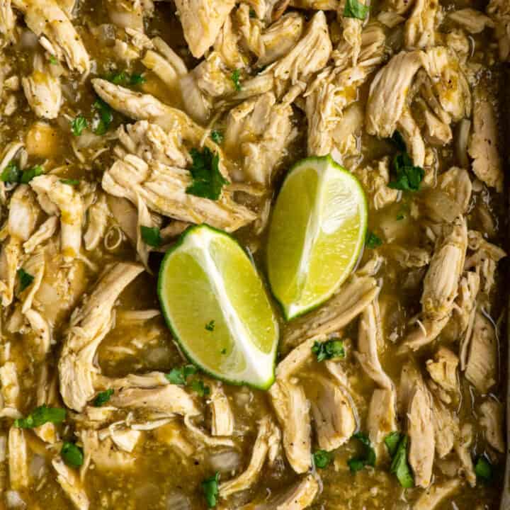 Close up of salsa verde chicken in a Crock Pot with garnished with cilantro and limes.