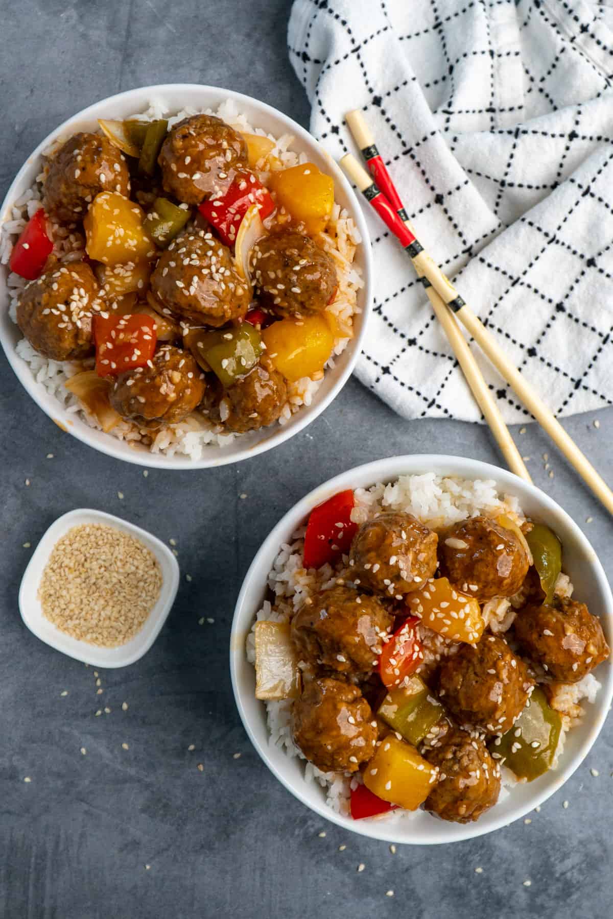 Overhead look at two white bowls of Crock-Pot sweet and sour meatballs garnished with sesame seeds.