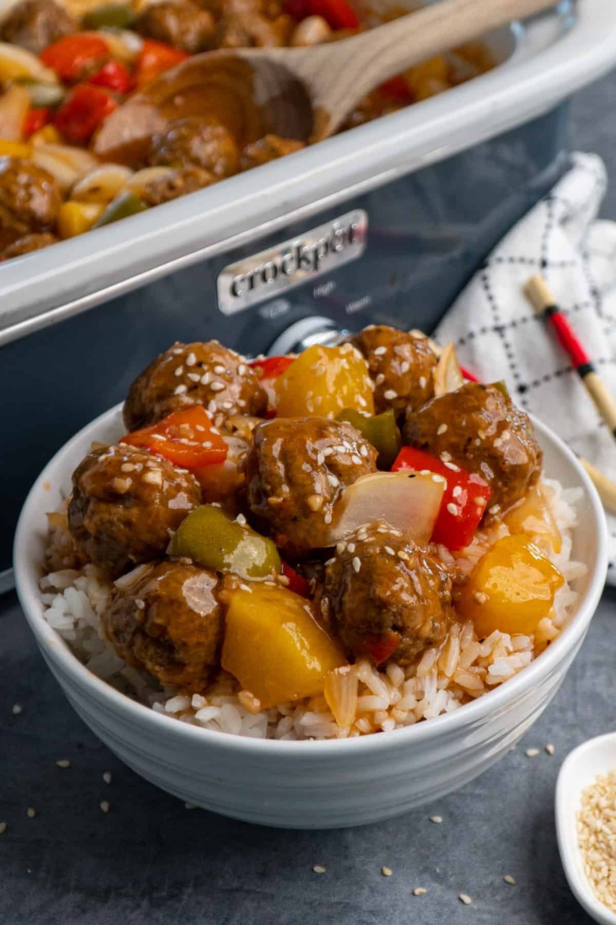 Close up of Crock-Pot sweet and sour meatballs over rice in a white bowl and garnished with sesame seeds.