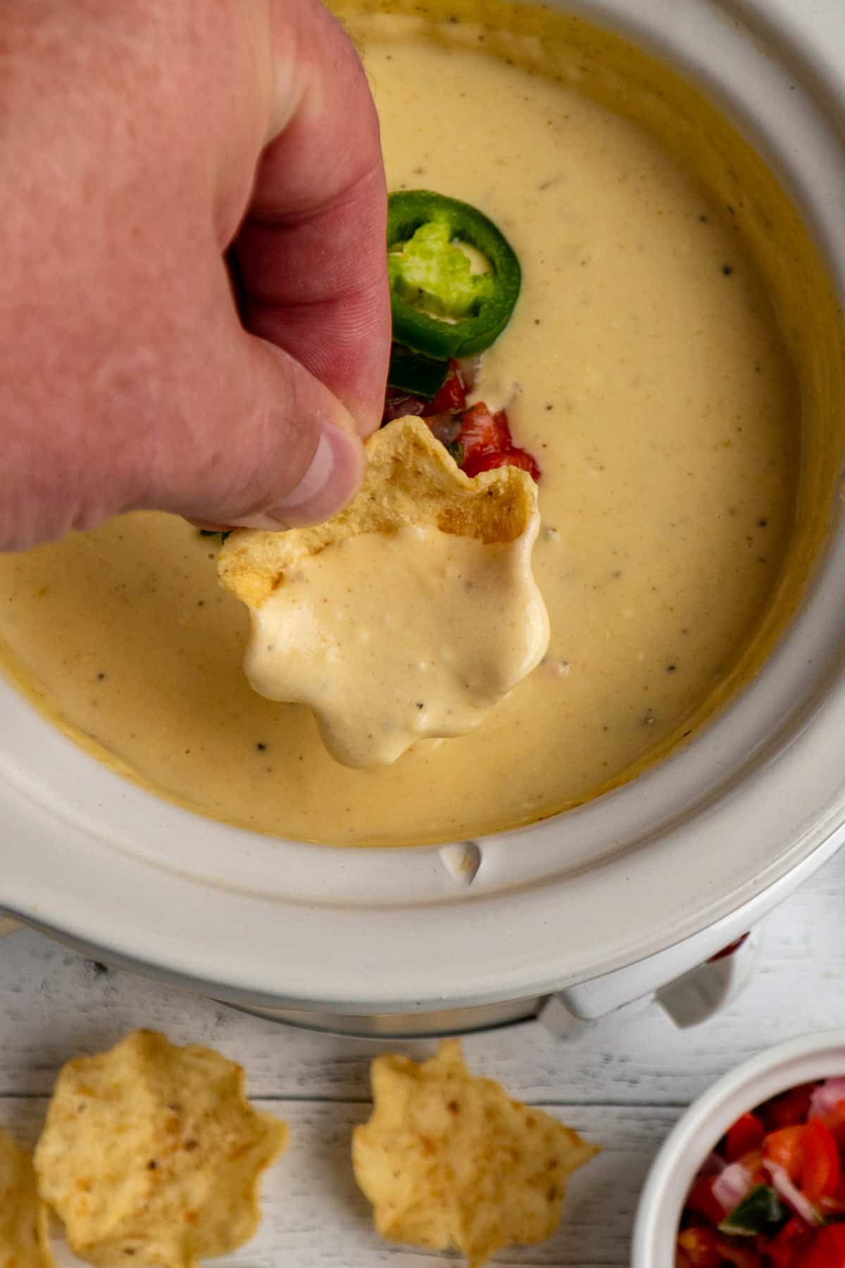 Close up of Crock-Pot white Queso dip on a chip that a hand is holding.