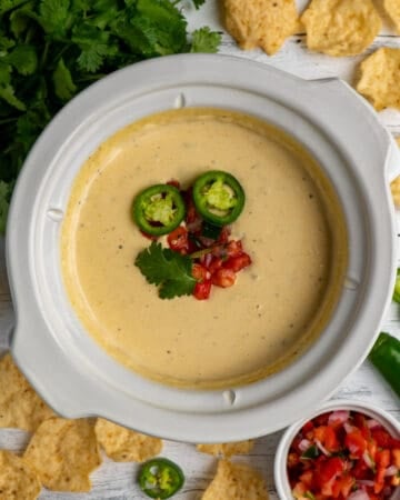 Overhead look at white queso dip in a slow cooker with pico de gallo on top.