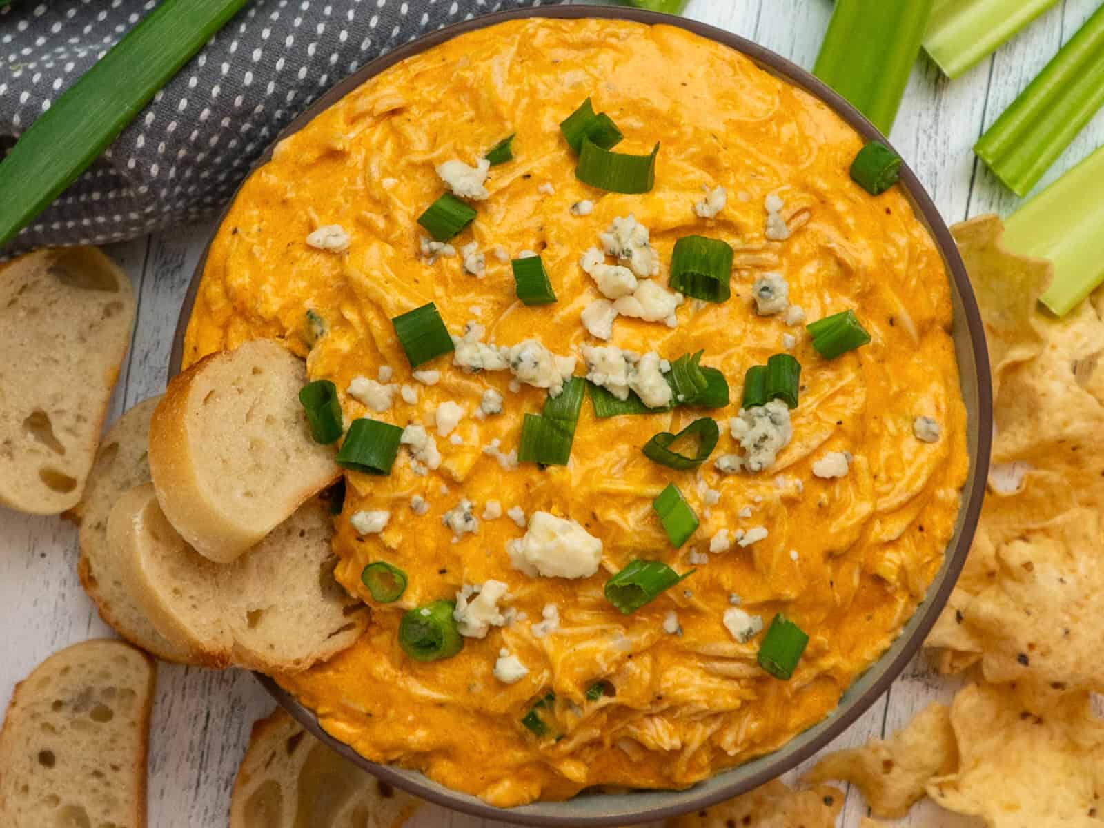 Buffalo chicken dip in a bowl and surrounded by sliced baguettes, chips and celery.
