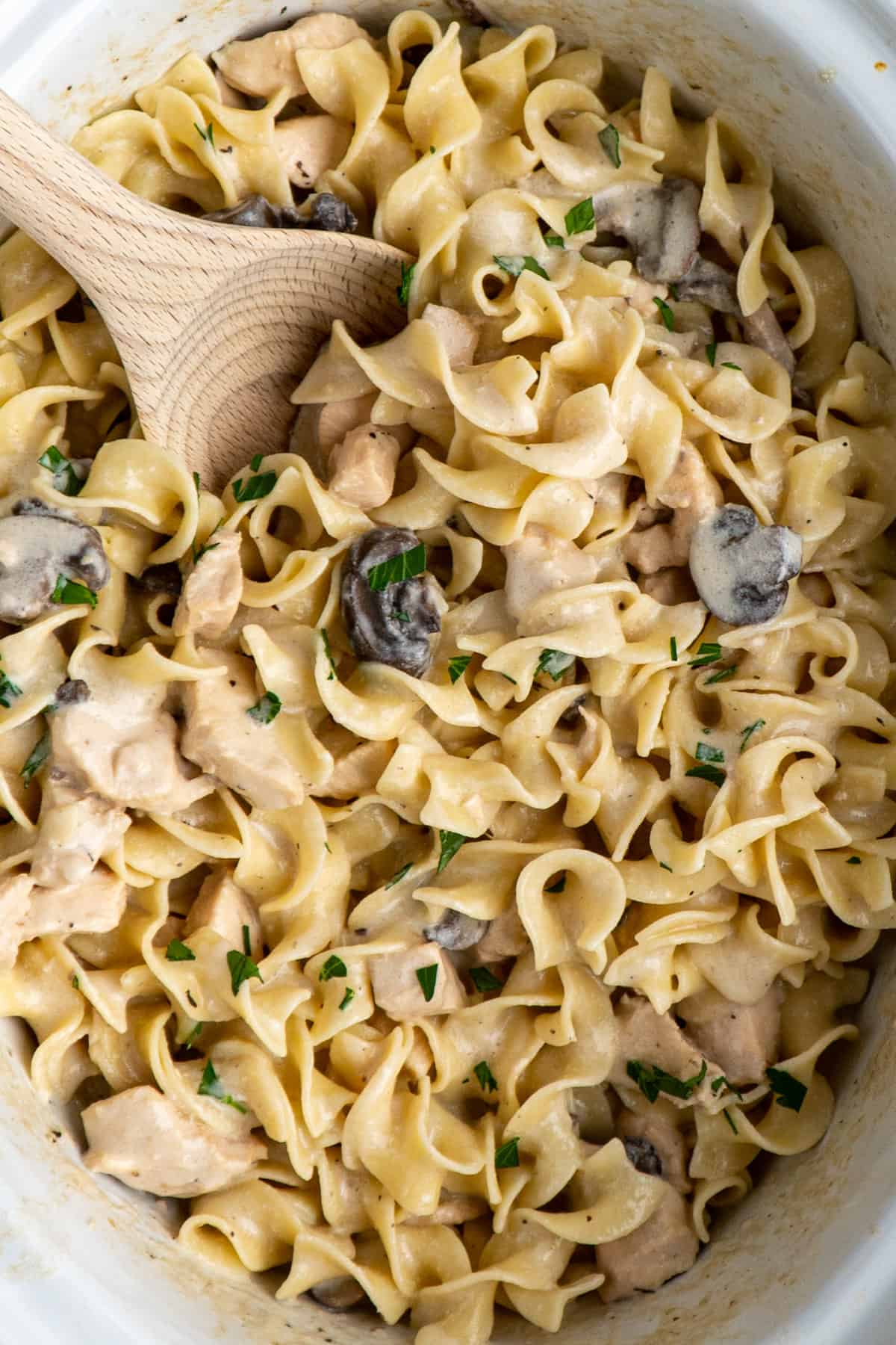 Chicken stroganoff in a crock pot with a wooden spoon and fresh chopped parsley.