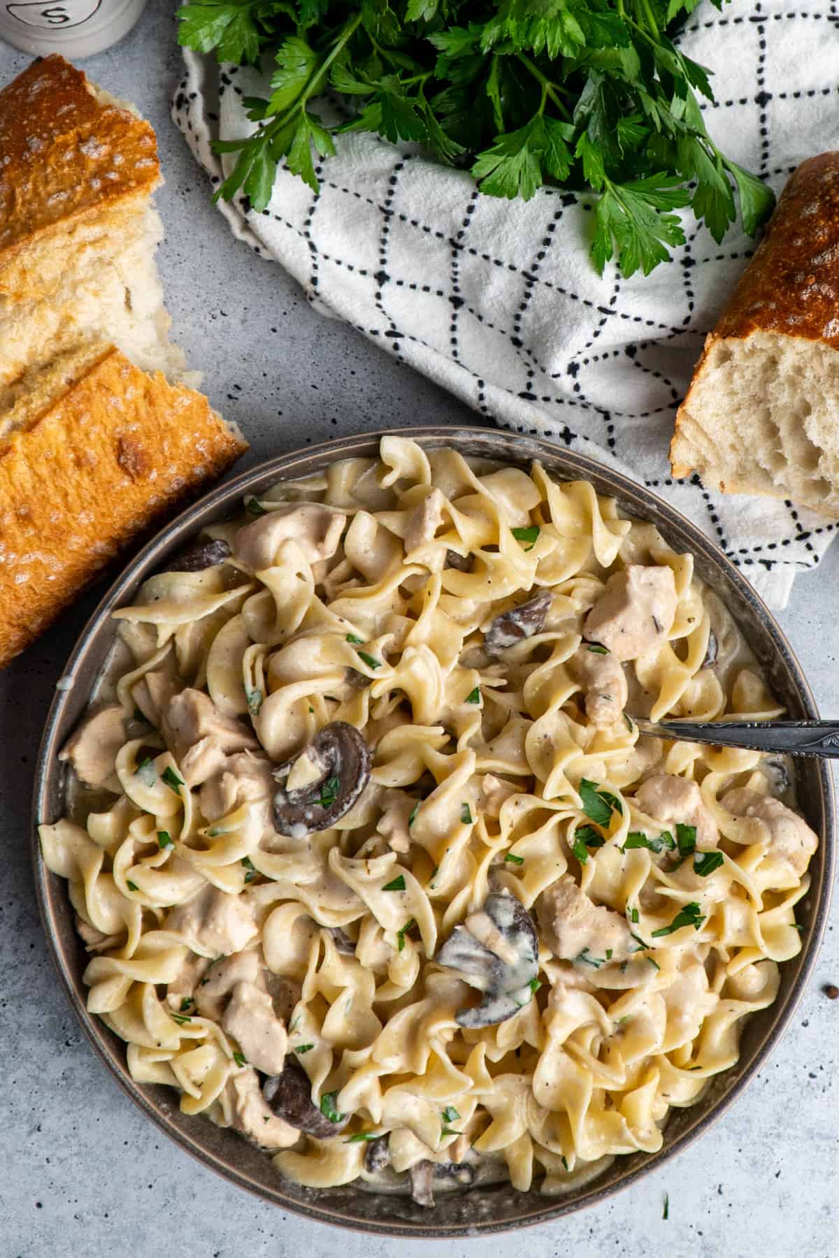 Slow cooker chicken stroganoff in a gray bowl and bread and parsley in the background.