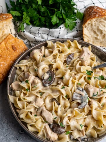 Slow cooker chicken stroganoff in a gray bowl and bread and parsley in the background.