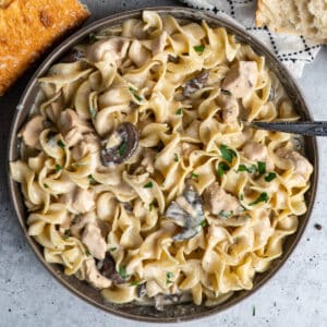 Slow cooker chicken stroganoff in a gray bowl and bread and parsley in the background.