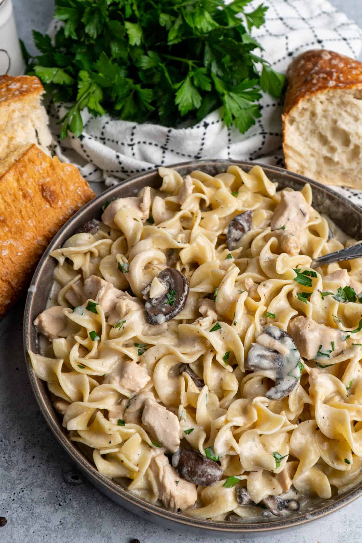 Slow cooker chicken stroganoff in a gray bowl and bread and parsley in the background.