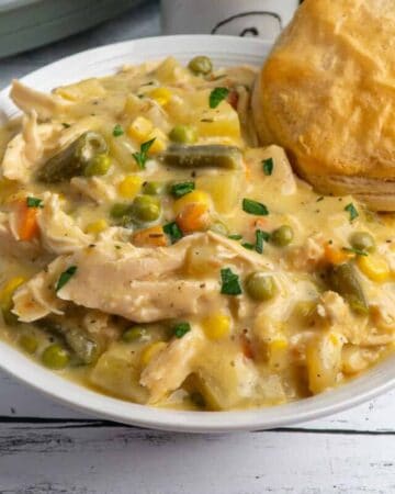Crock Pot chicken pot pie in a white bowl with a biscuit in it and a slow cooker in the background.
