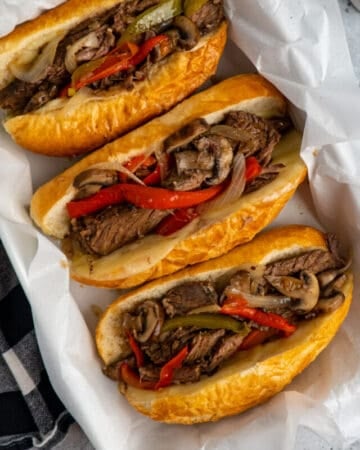 Crock Pot Philly cheesesteak sandwiches in a baking dish lined with parchment paper.