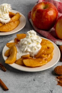 Close up of Cracker Barrel fried apples on a white plate with whipped cream on top.