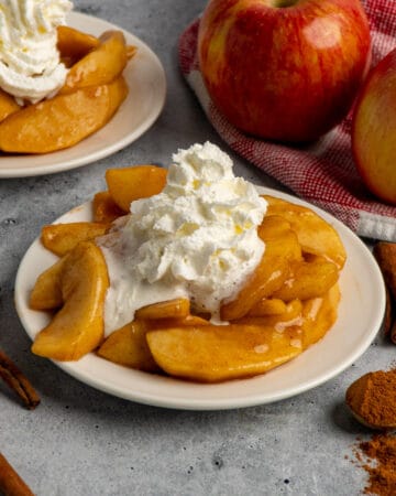 Close up of Cracker Barrel fried apples on a white plate with whipped cream on top.