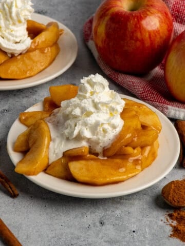 Close up of Cracker Barrel fried apples on a white plate with whipped cream on top.