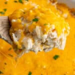 A wood spoon holding crock pot cheesy hash browns over a slow cooker.