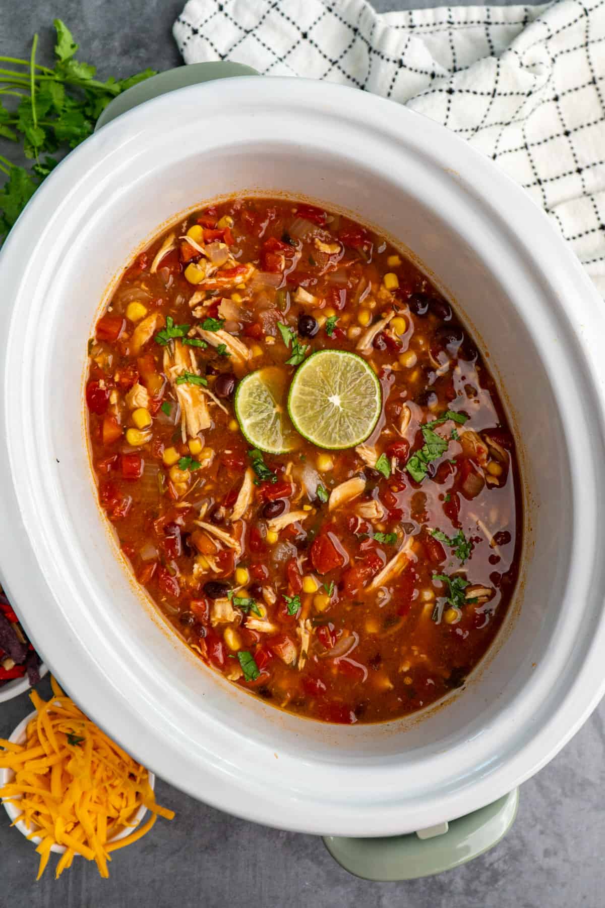 Crock Pot chicken tortilla soup in a slow cooker with cilantro and limes on top.