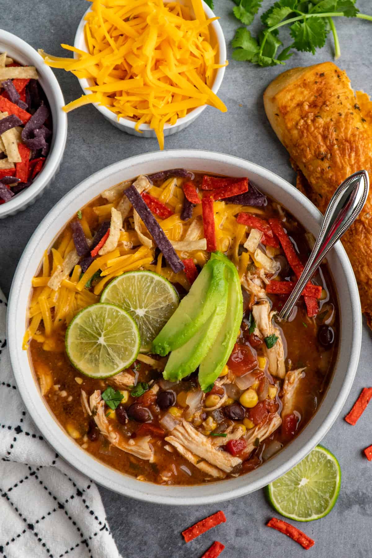 Crock Pot chicken tortilla soup in a bowl with limes and sliced avocado on top and cheese in the background.