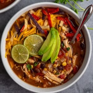 Crock Pot chicken tortilla soup in a bowl with limes and sliced avocado on top.