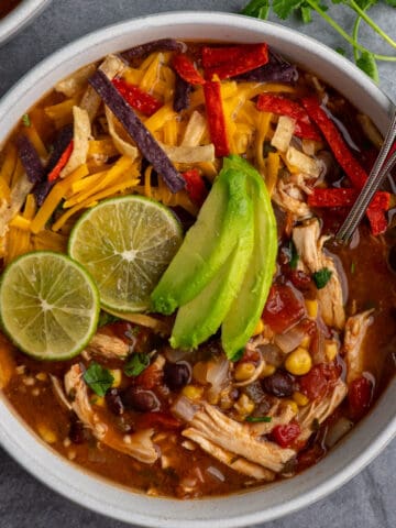 Crock Pot chicken tortilla soup in a bowl with limes and sliced avocado on top.
