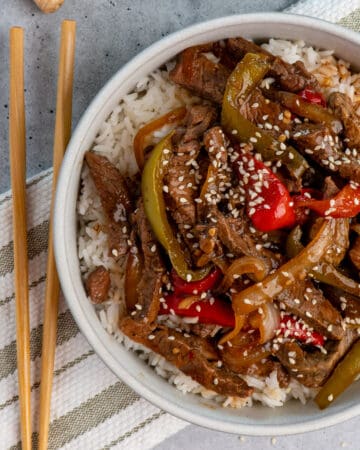 Image of crock pot pepper steak over white rice in a bowl.