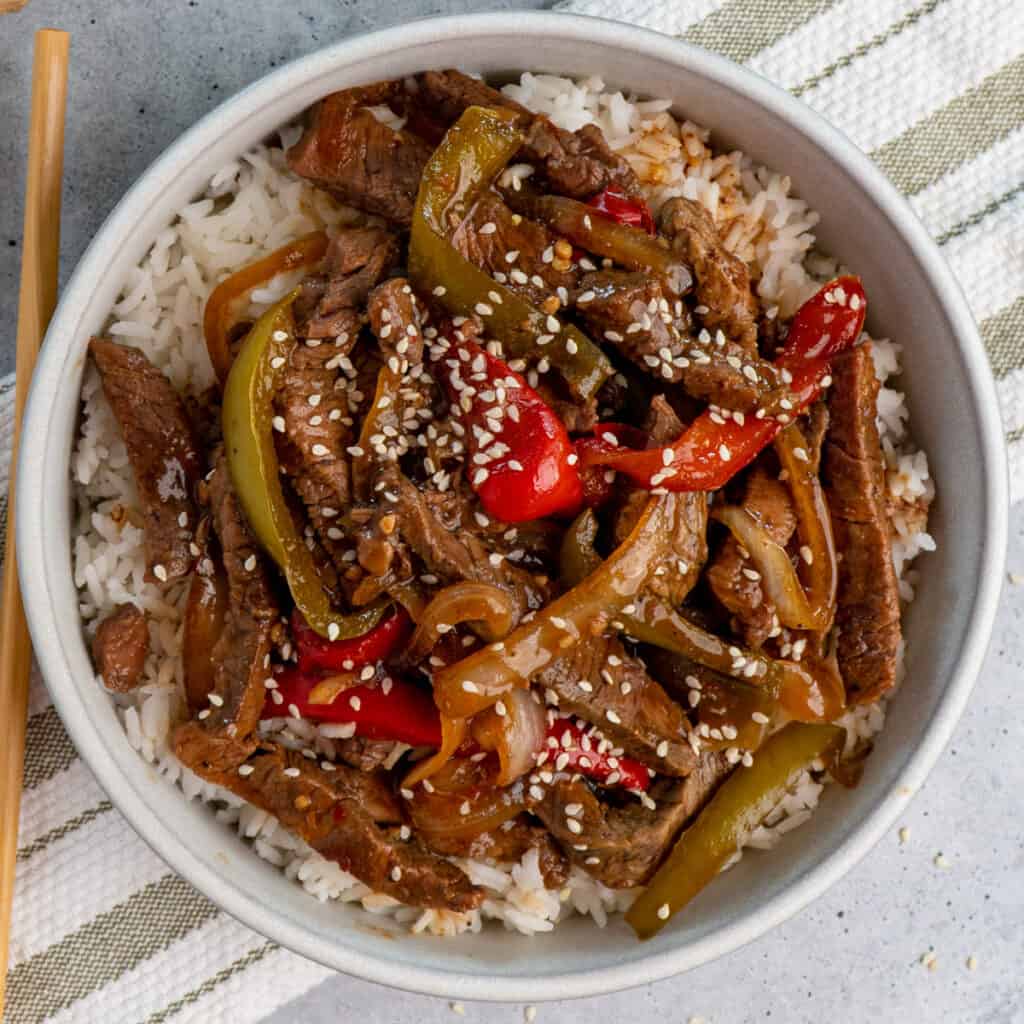 Crock pot pepper steak over white rice in a bowl.