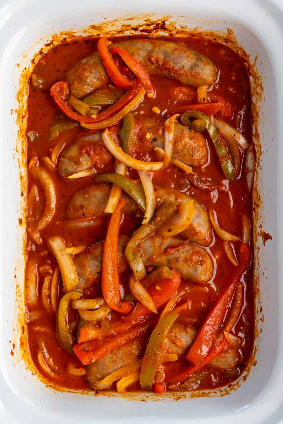Overhead look at sausage and peppers inside a white slow cooker.