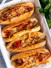 Overhead look at crock pot sausage and pepper in hoagies covered in cheese inside a baking dish.