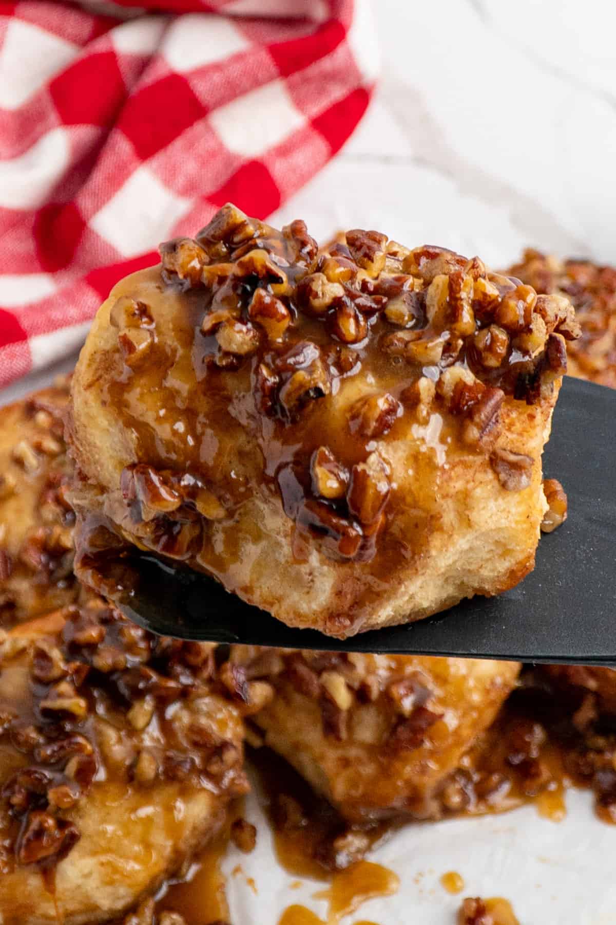 Overhead look at Crock Pot sticky buns on parchment paper with one being held up with a spatula.
