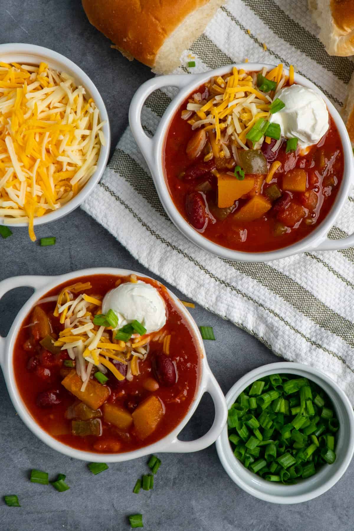 Two white bowls of slow cooker butternut squash chili topped with cheese and sour cream.