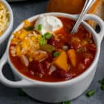Close up of slow cooker butternut squash in a white bowl topped with cheese and sour cream.