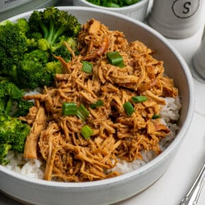 Close up of slow cooker honey garlic chicken in a bowl over rice with broccoli.