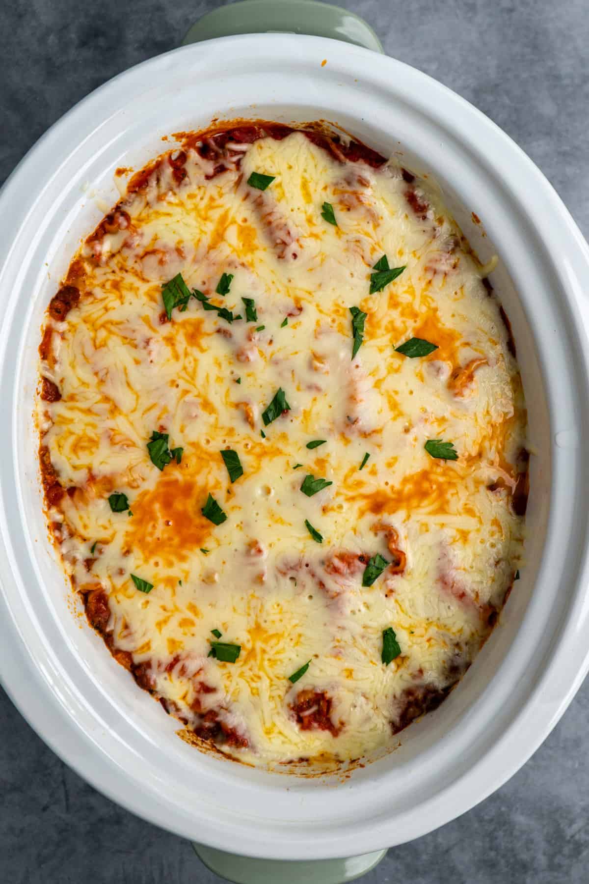 Overhead look at lasagna in a slow cooker with fresh parsley on top.