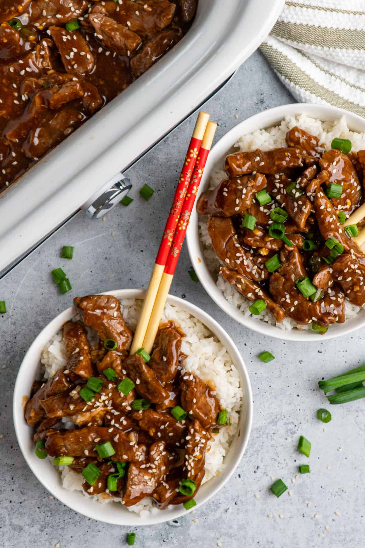 Two white bowls with slow cooker teriyaki beef over rice and garnished with green onions.