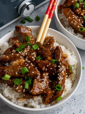 Close up of slow cooker teriyaki beef over white rice with chopsticks in it.
